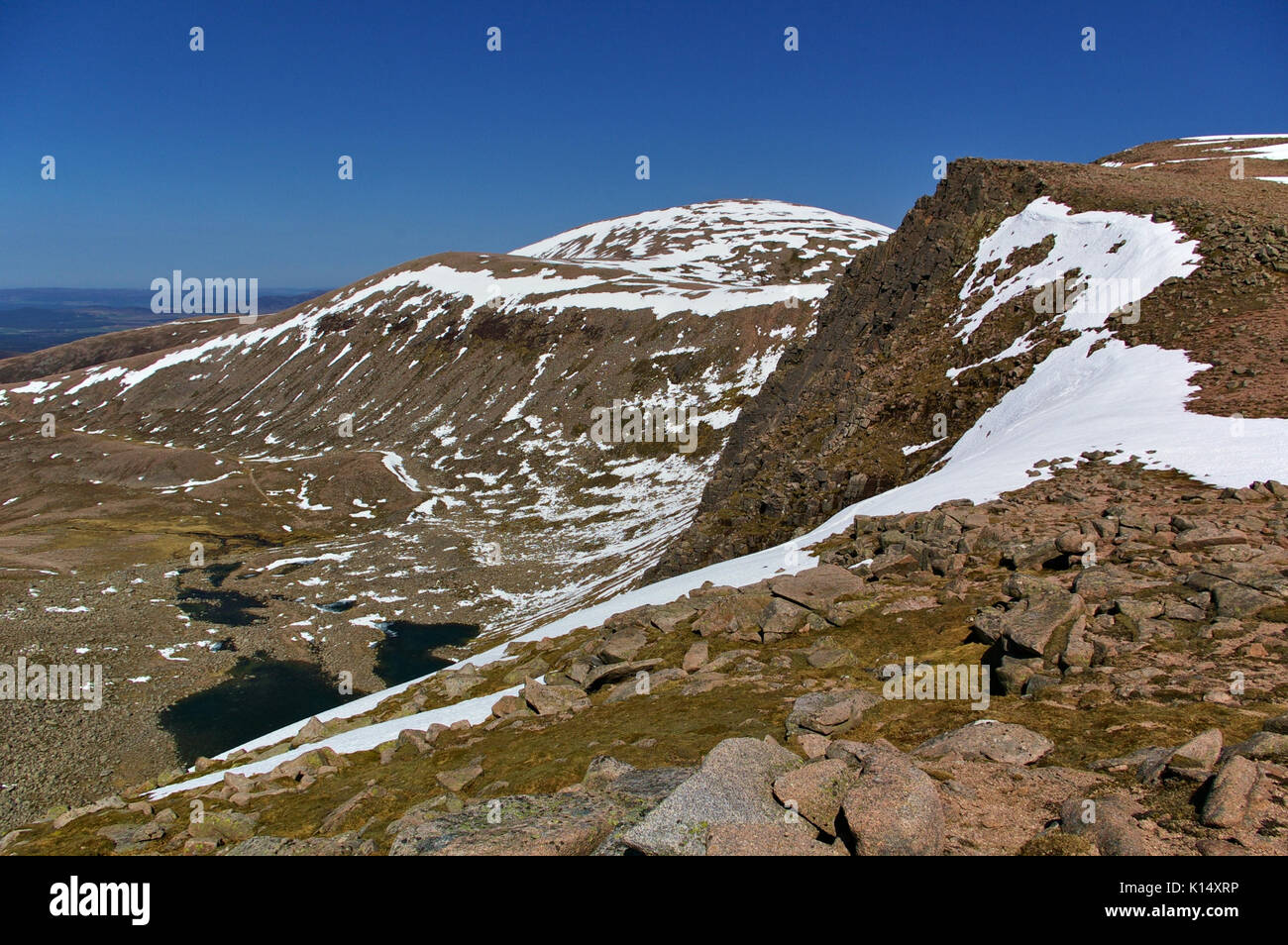 Auf dem Gipfel des Cairn Gorm mit Tal, steilen Hängen, Steine, Schnee, Seen unter Stockfoto