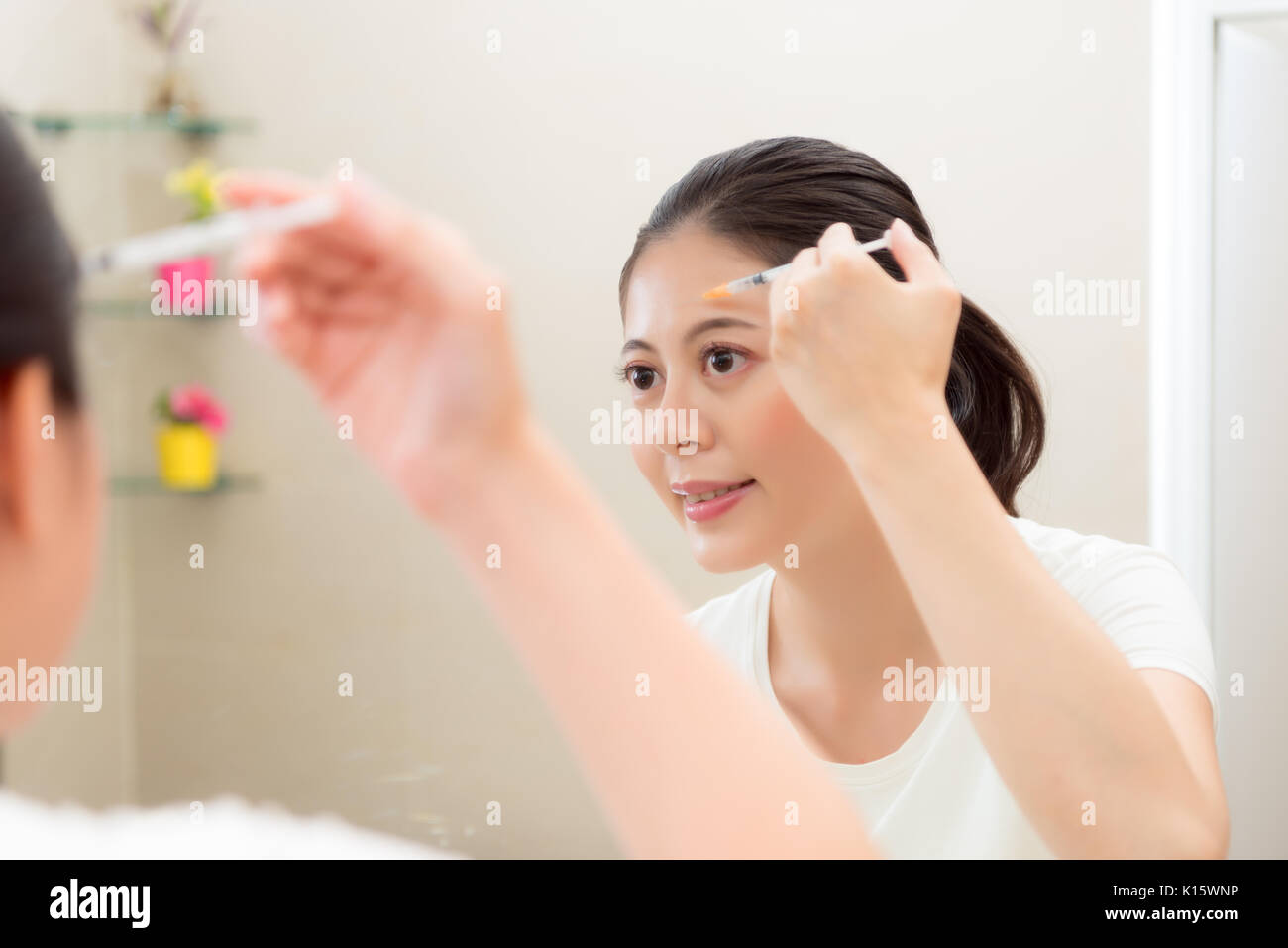 Lächelnd schöne Frau im Spiegel Reflexion Bild mit der Spritze Injektion Beauty Care Medizin in Stirn steht auf Bad zu Hause suchen. Stockfoto