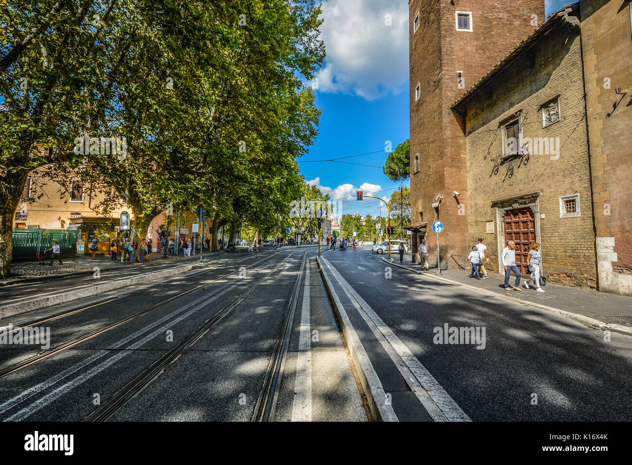 Eine breite Straße mit Titel und Linien in der Straße Bäume Überhang und Touristen zu Fuß auf dem Gehweg in Rom Italien Stockfoto