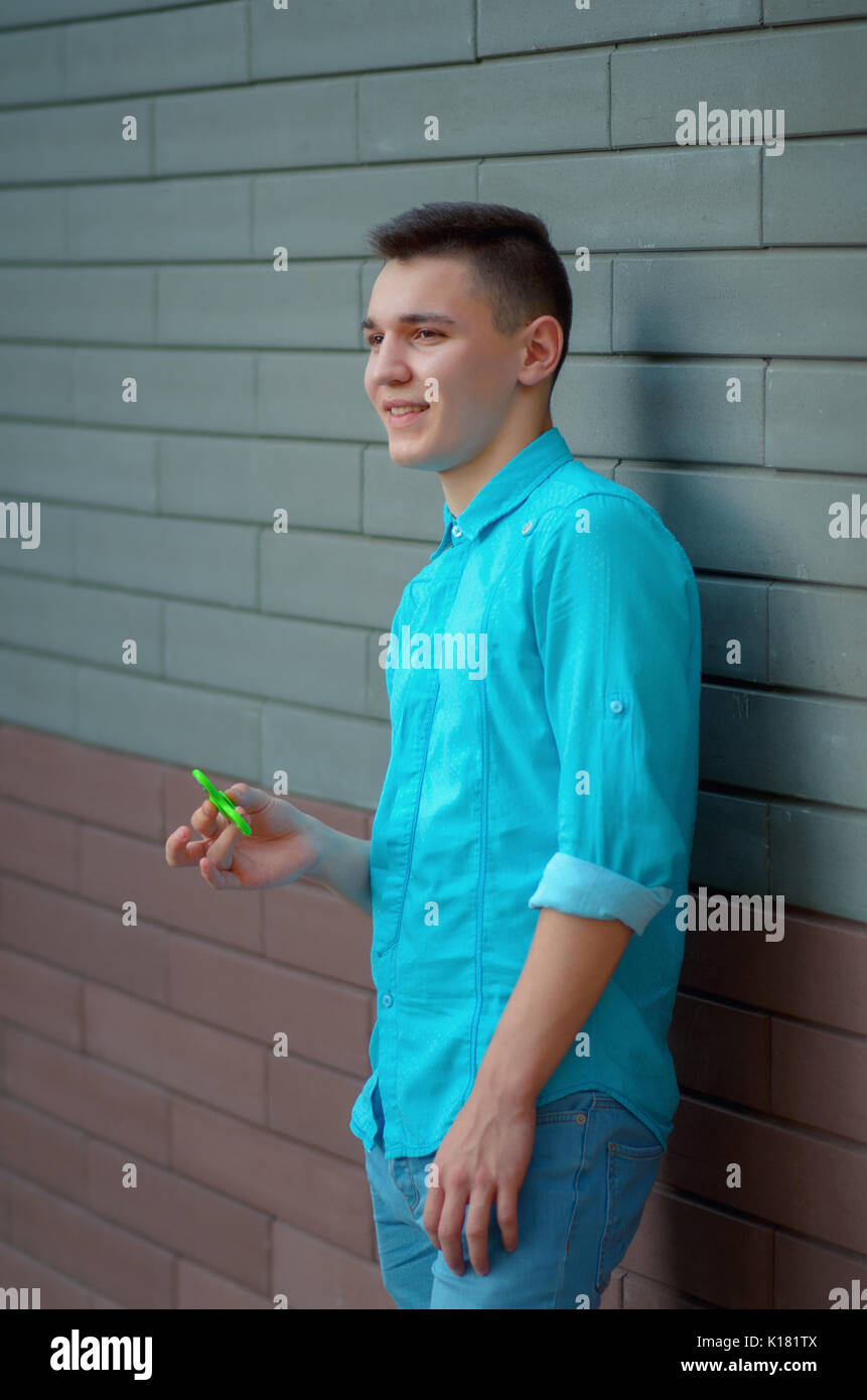 Stilvolle Teenager auf der Azure T-Shirt und Blue Jeans Hand beliebte Gadget zappeln Spinner. Mann spielt mit grünen Spinner im Freien auf der Brick Stockfoto