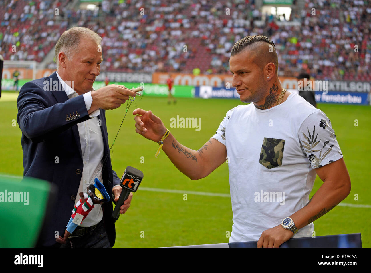 26.08.2017, Fussball 1. Liga 2017/2018, 2. Spieltag, FC Augsburg - Borussia Mönchengladbach, in der Wwk-Arena Augsburg. Ex-Augsburger Raul Bobadilla (re, Gladbach) wird vom FCA mit Figur aus der Augsburger Puppenkiste (Jim Knopf) verabschiedet, li: Sportdirektor Stefan Reuter (FC Augsburg) Foto: Cronos/MIS Stockfoto