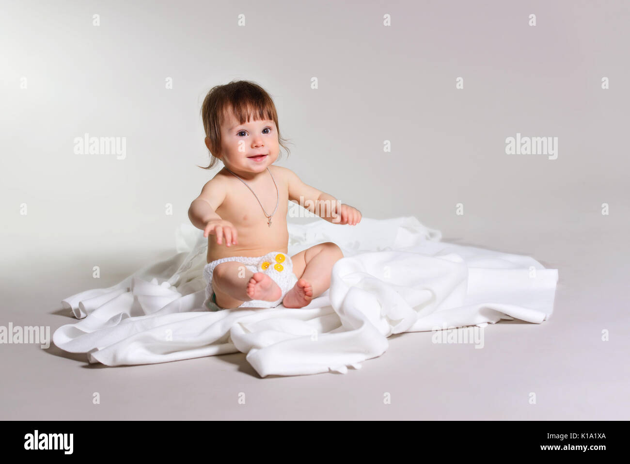 Kleines Mädchen sitzt auf einer weißen Decke in die Kamera schaut. Stockfoto