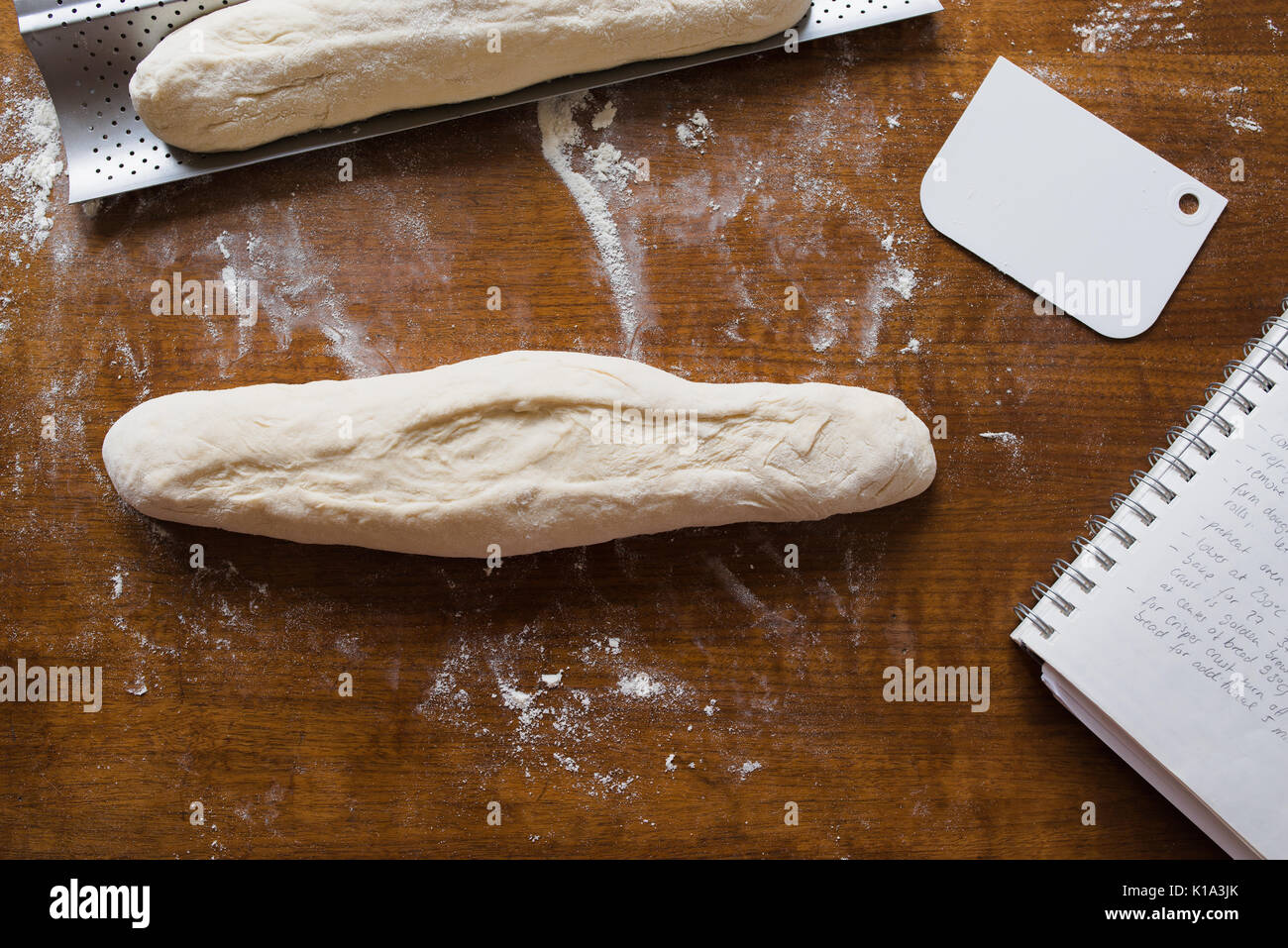 Hausgemachte französische Baguette über die in den Ofen mit Rezeptbuch und Teig Abstreifer auf Holz- Hintergrund gehen Stockfoto