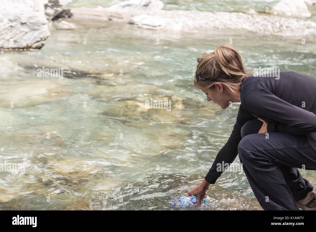 Eine Frau oder ein Mädchen füllt eine Flasche Wasser aus einer kristallklaren Fluß oder Strom in Neuseeland Stockfoto