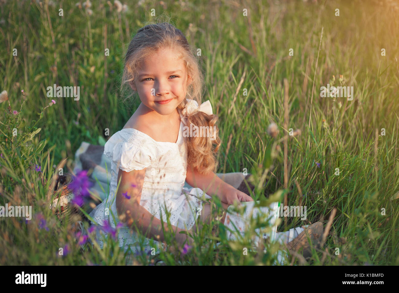 Kleines Mädchen mit einem Buch in der Hand auf einer Wiese in einem Sommer sonnigen Tag. Stockfoto
