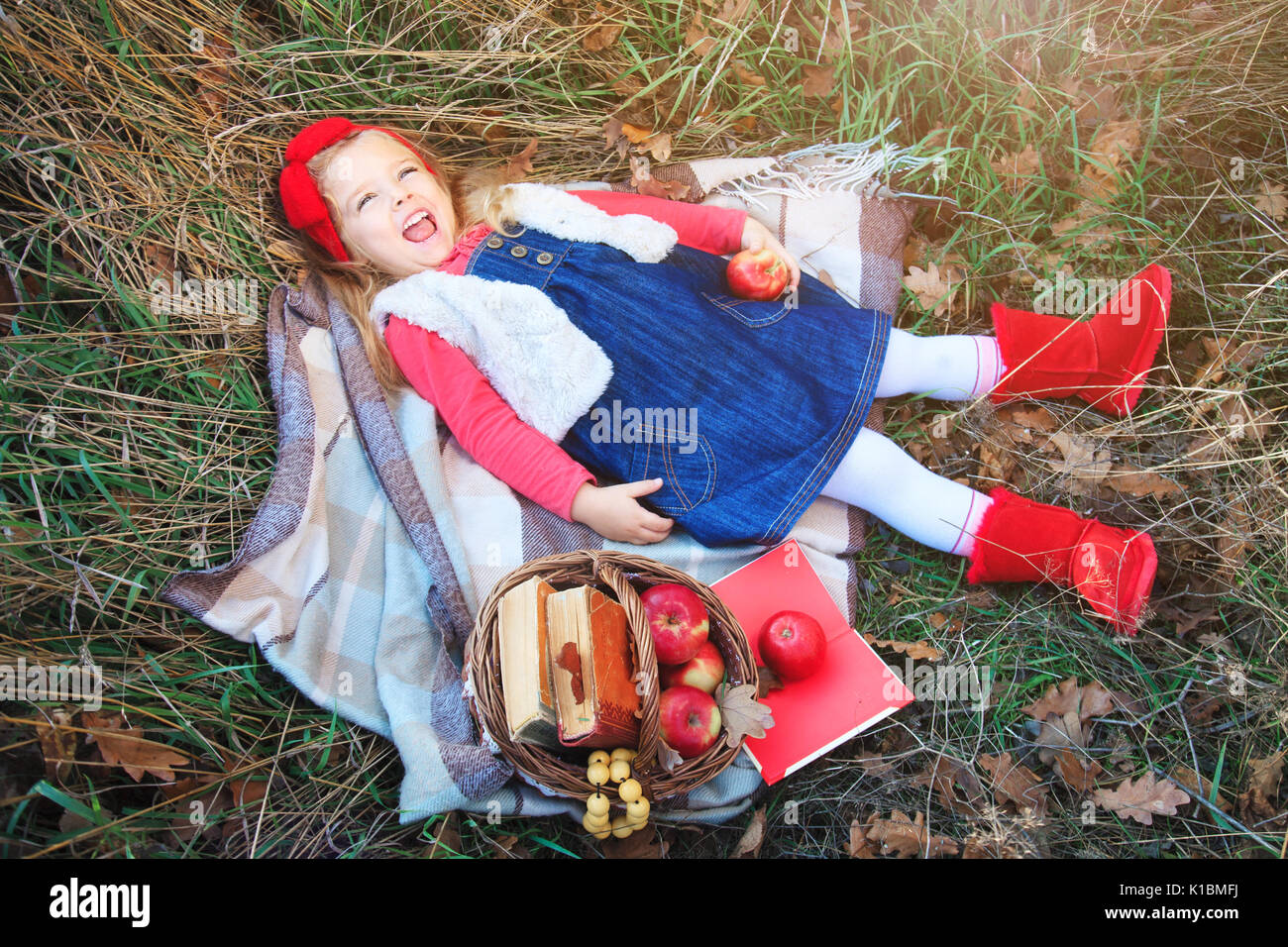 Kleines Mädchen liegt im Gras auf einem Plaid mit einem Korb mit Früchten im Herbst Tag. Stockfoto
