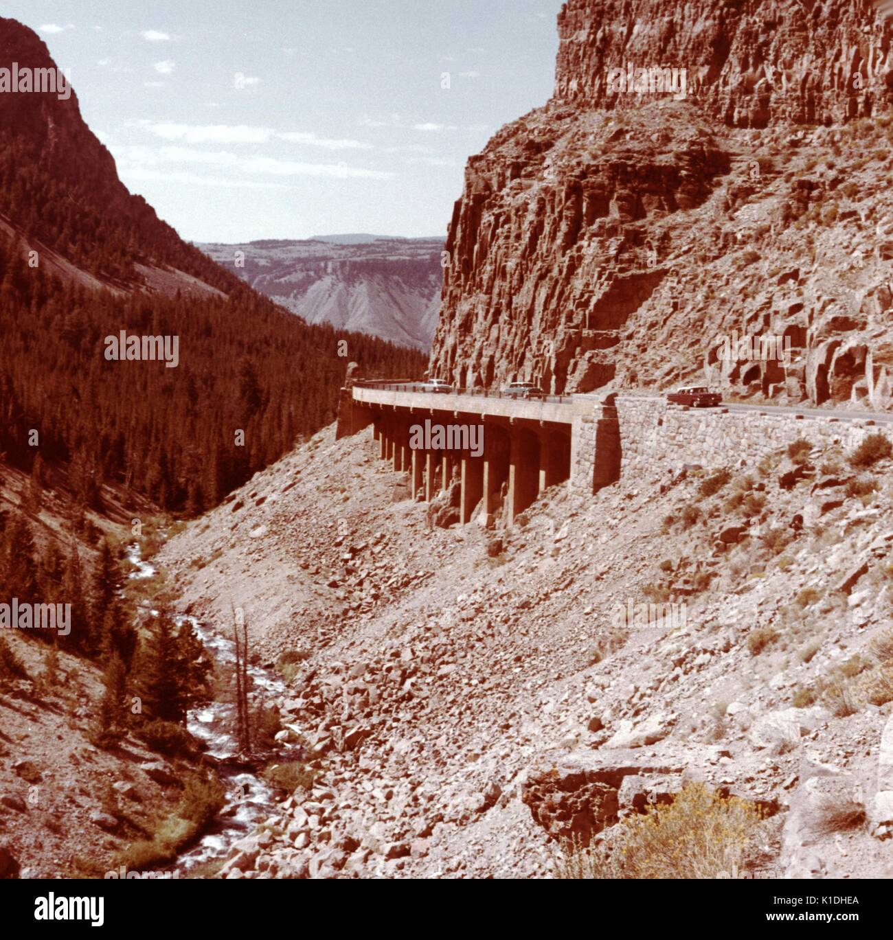 Ein Schuss durch die Golden Gate Canyon, von der Straße, Autos können gesehen werden Verfahren eine Brücke, die auf einem Hügel liegt, mit einem kleinen Fluss und einer anderen Hügel gegenüber, Colorado, 1975. Stockfoto