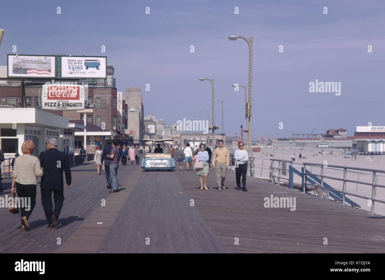 Touristen, die auf der Promenade in Atlantic City, New Jersey, mit Schildern Werbung Coca Cola, ein Computer-Drucker und ein Pizza-Restaurant, Strand sichtbar, 1975. Stockfoto