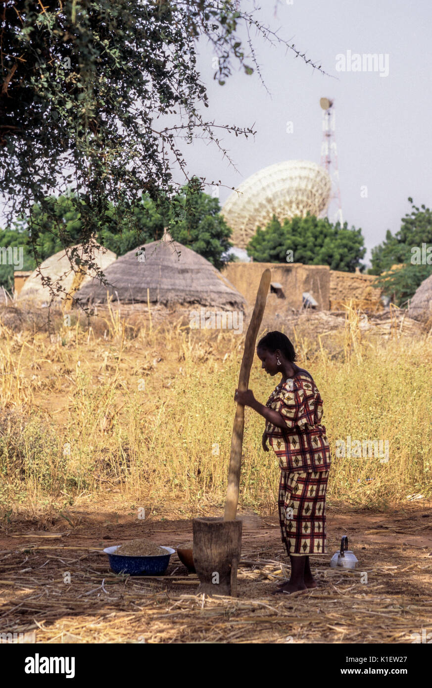 Niger, Westafrika, Frau Pfund Hirse für Abendessen. Satellitenschüssel die Übertragung von Niger internationale Telefongespräche im Hintergrund. Stockfoto