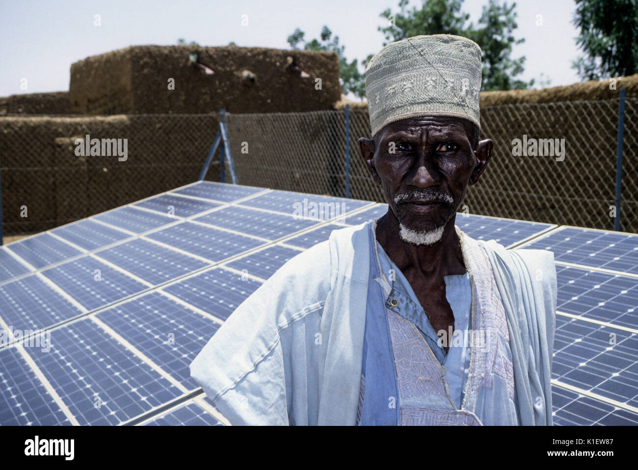 Niger, Kantche, West Afrika. Ein Dorfältester, mit Solarzellen im Hintergrund für die Stromversorgung Dorf Wasserpumpe. Stockfoto