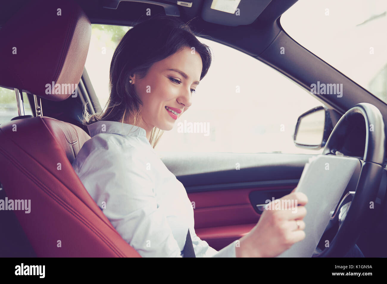 Transport und Ownership Konzept. Junge attraktive Frau im neuen Auto lesen Signatur von Dokumenten Stockfoto
