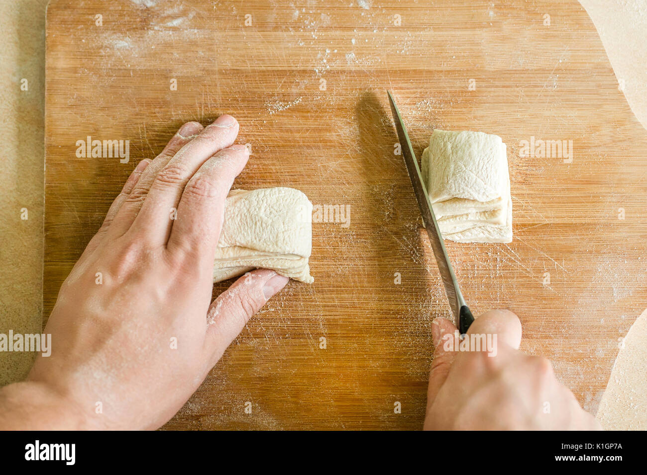 Ansicht von oben Schießen von Menschenhänden Schneiden von rohem Teig auf dem Tisch Stockfoto