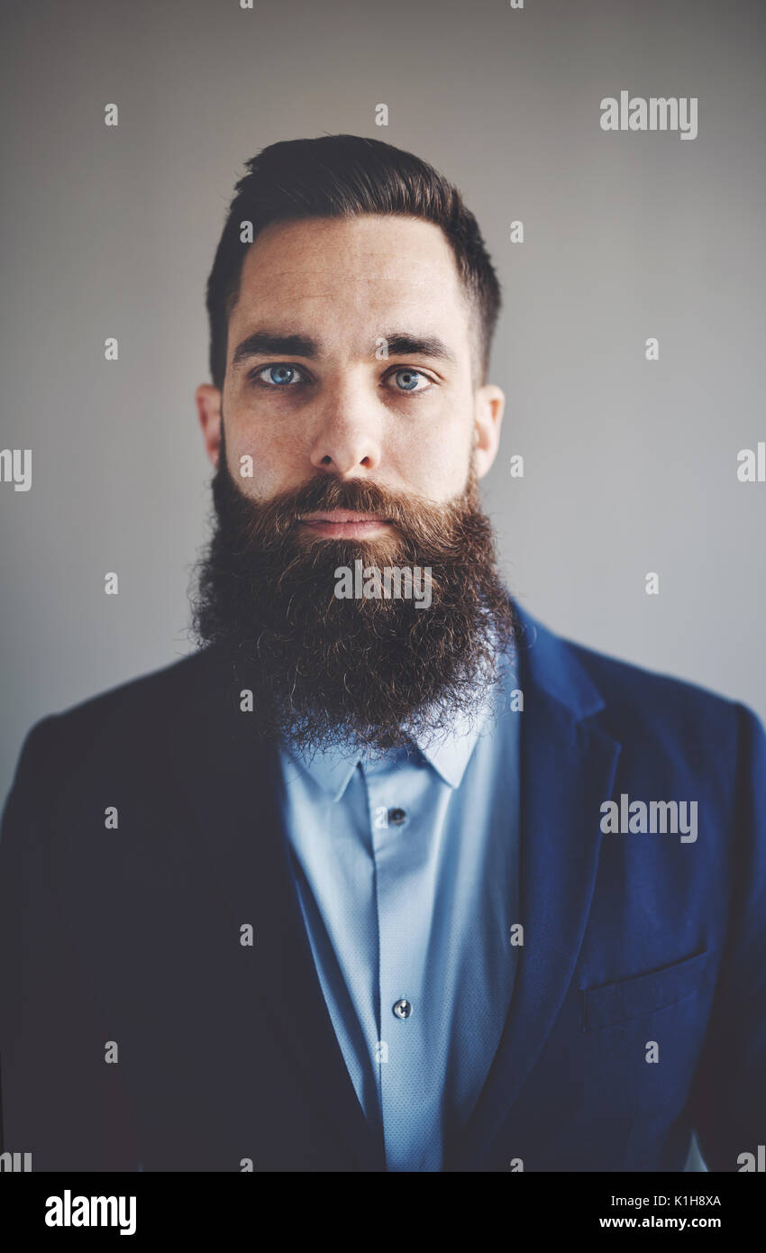 Porträt einer selbstbewussten jungen Geschäftsmann mit langem Bart und trägt einen Blazer, die alleine stehen in einem Büro Stockfoto