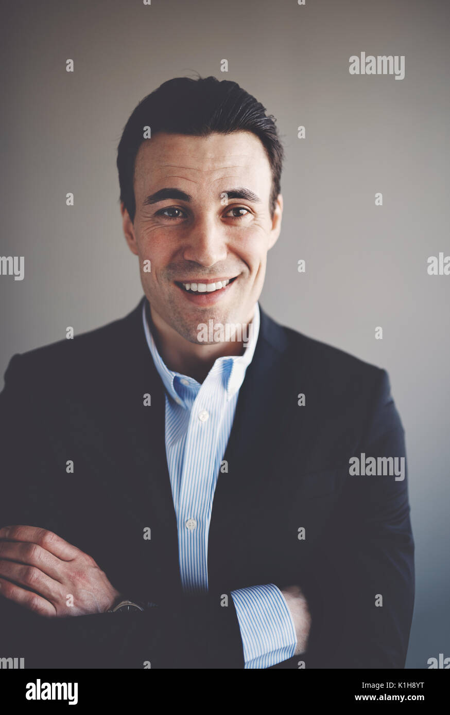 Porträt einer selbstbewussten jungen Geschäftsmann trägt einen Blazer, die alleine stehen in einem Büro mit verschränkten Armen Stockfoto