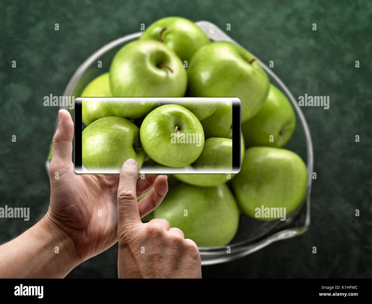 Zwei Hände, die ein mobiles Smartphone und ein Bild von grünen Äpfeln nehmen Stockfoto