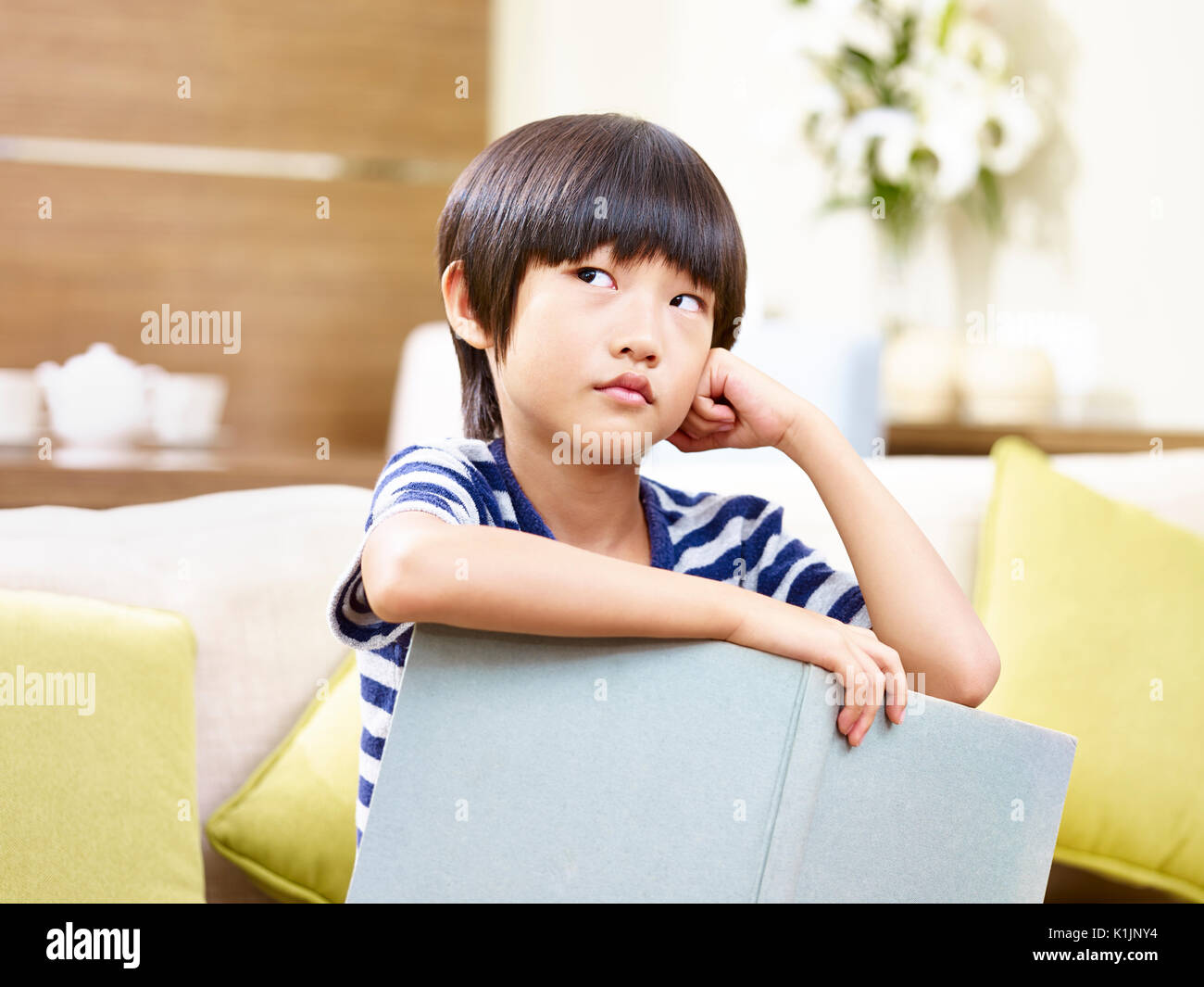 Kleine asiatische Kind sitzen auf der Couch, die ein Buch suchen und Denken. Stockfoto
