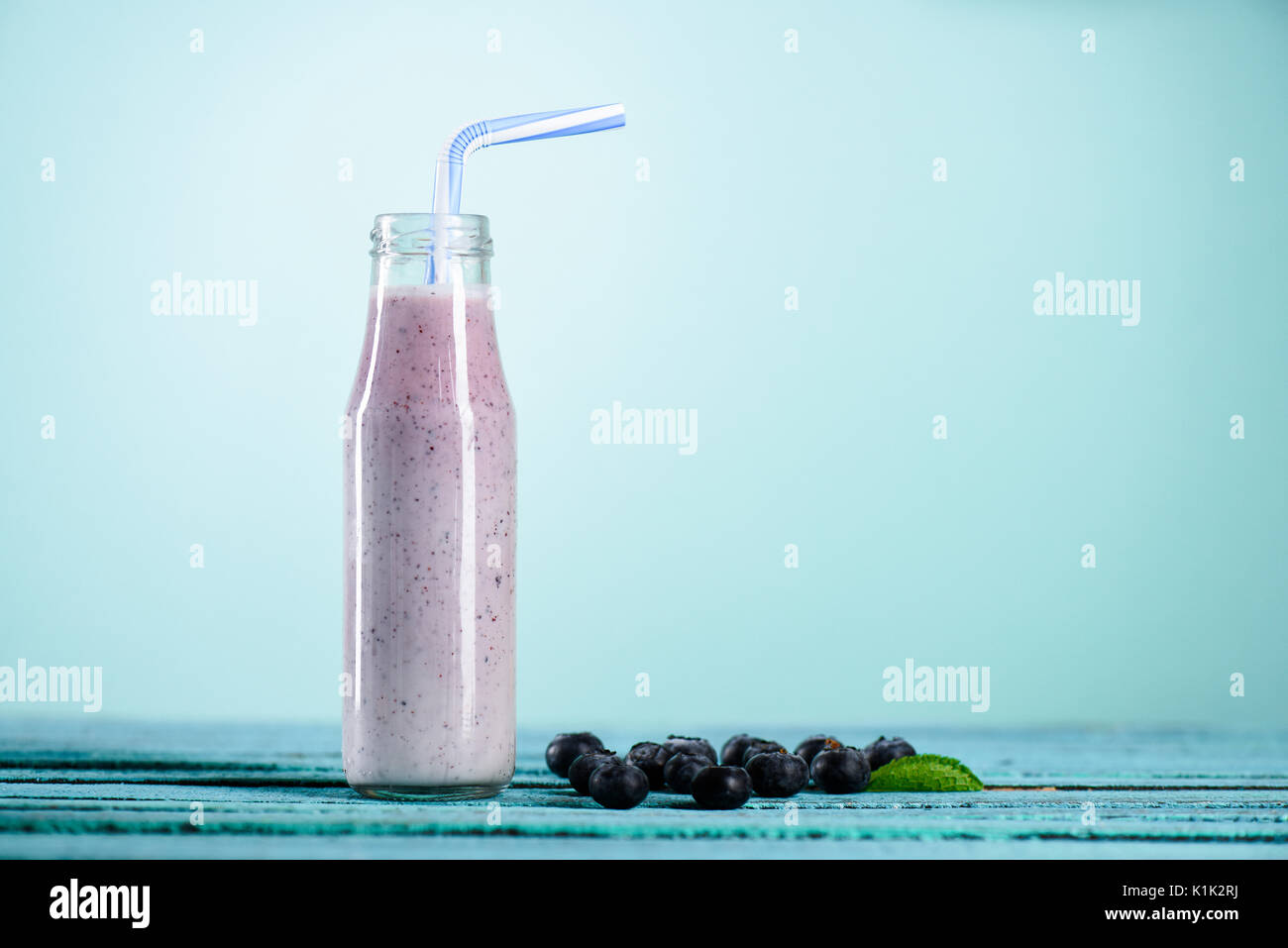 Hausgemachten blueberry Milchshake in Glasflasche mit Stroh auf der Tischplatte auf Blau Stockfoto