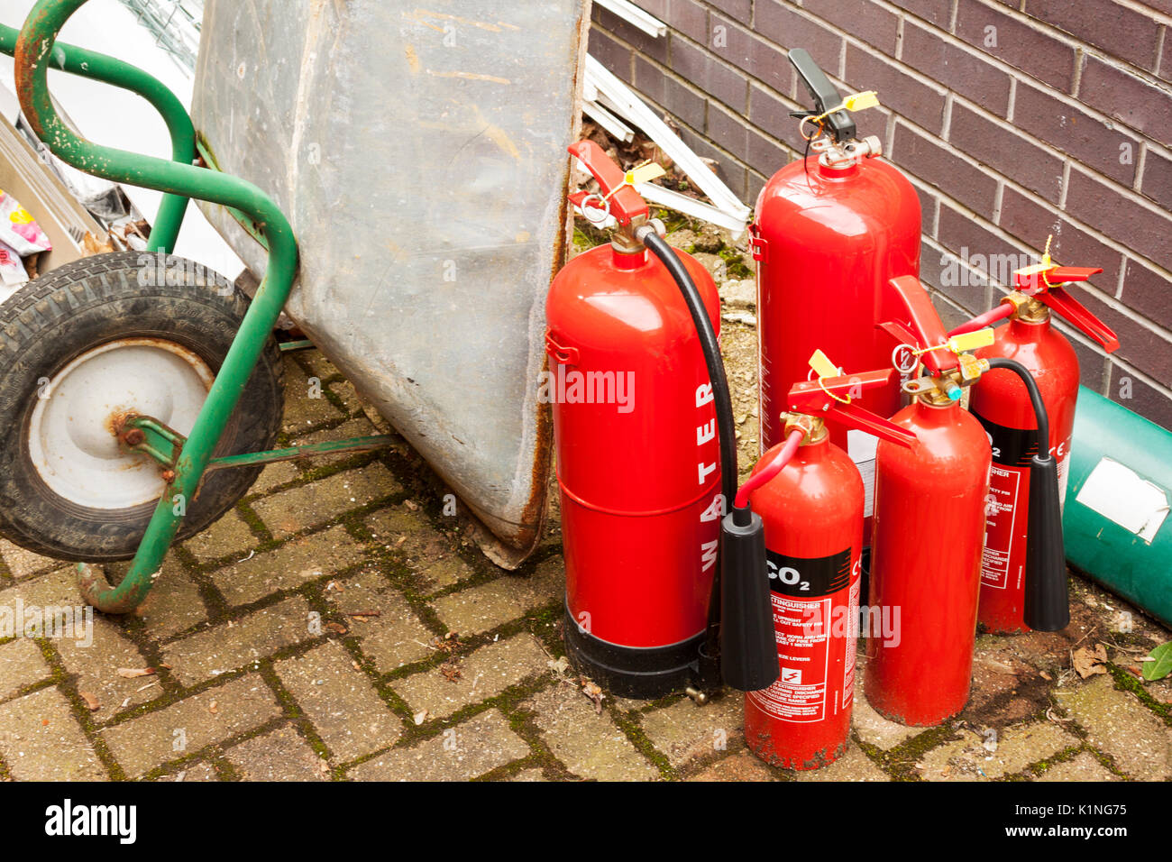 Alte verworfen Feuerlöscher in einem Bauherren Hof mit einem Rad Barrow und einen Haufen Müll Stockfoto