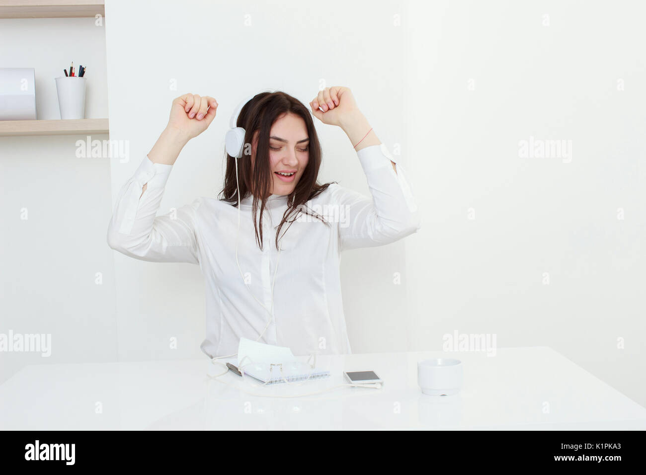 Schöne junge Frau sitzt am Schreibtisch und das Hören von Musik in Weiß Büro Stockfoto