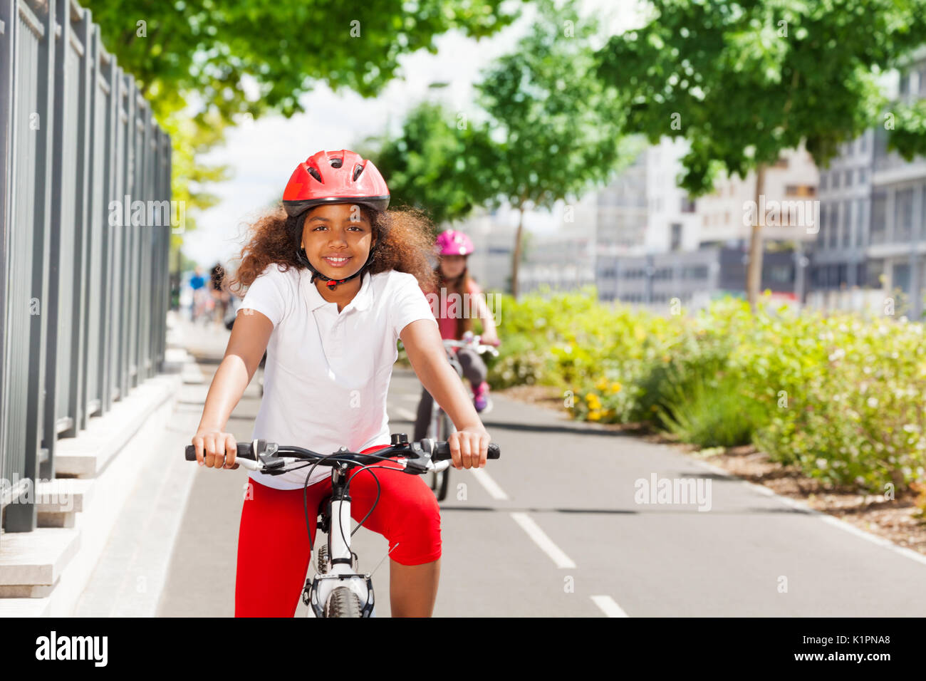 Portrait von Happy afrikanisches Mädchen in Sicherheit Helm reiten ihr Fahrrad auf Radweg im Sommer Stockfoto