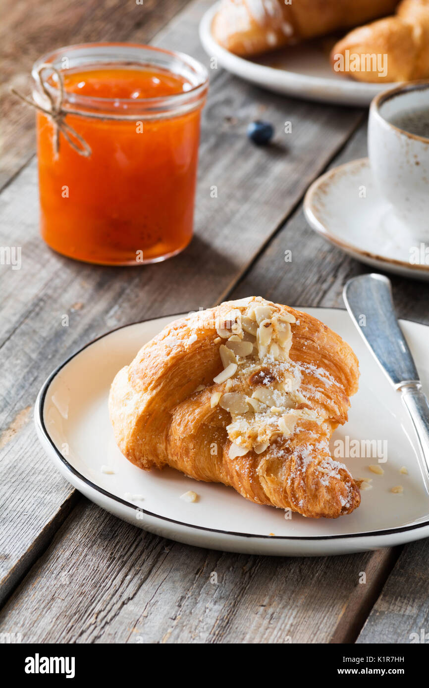 Kontinentales Frühstück Croissant, Marmelade im Glas und Tasse Kaffee auf Holztisch. Vertikale, selektiver Fokus Stockfoto