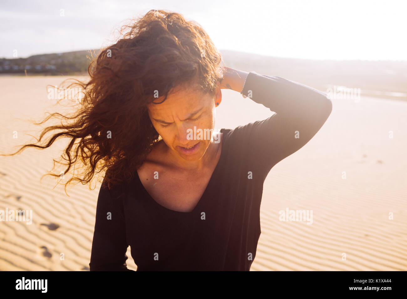 Mittleres Alter lockiges Haar weiß Frau um die 35, die von der intensiven Sonne und Wind in den Dünen von Jericoacoara, Ceará, Brasilien Stockfoto
