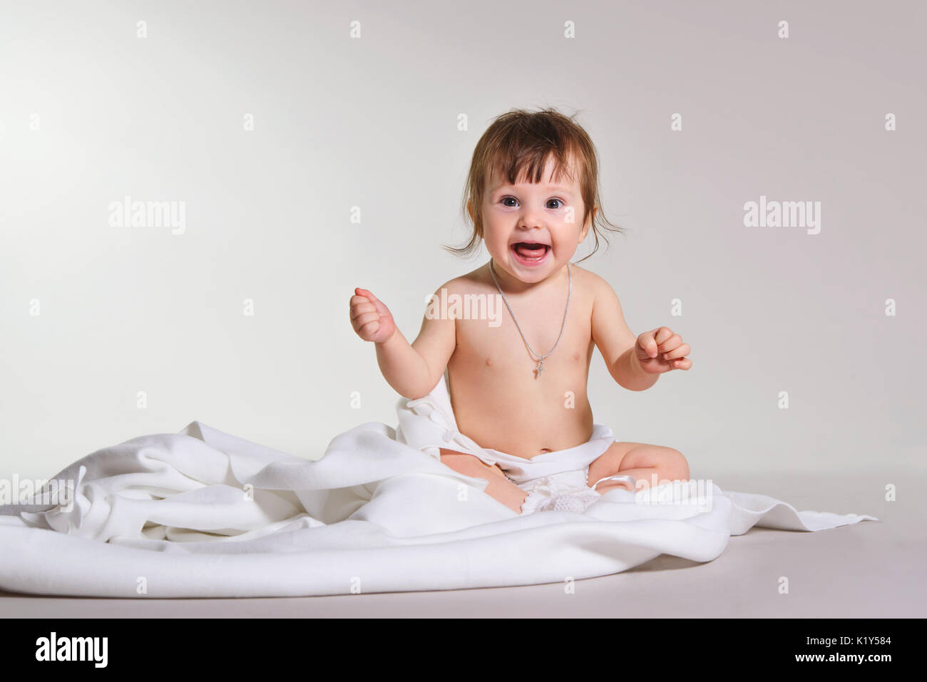 Kleines Mädchen sitzt auf einer weißen Decke in die Kamera schaut. Platz für Text. Stockfoto