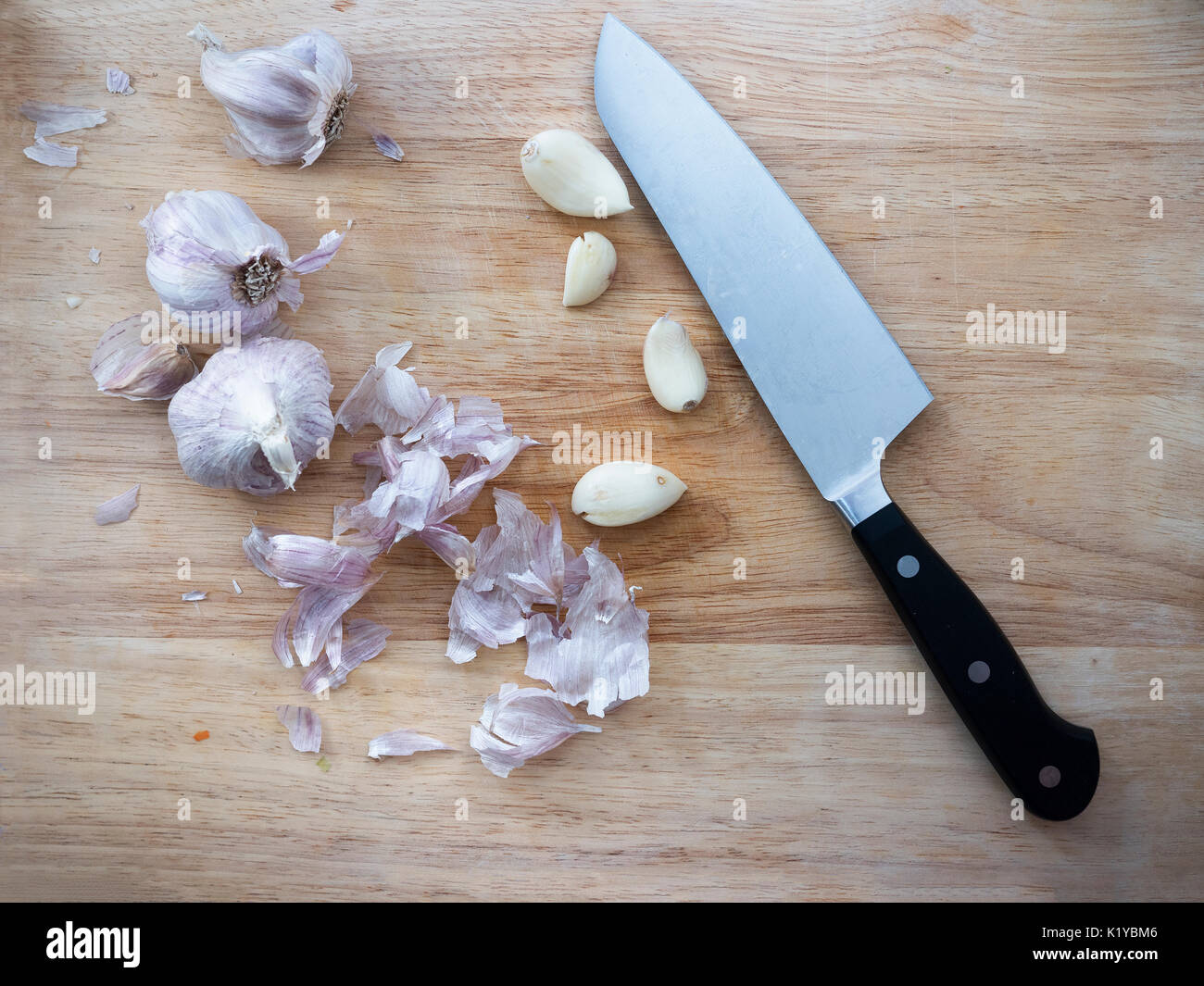 Knoblauchzehen und Zwiebeln auf Schneidebrett mit Messer Stockfoto