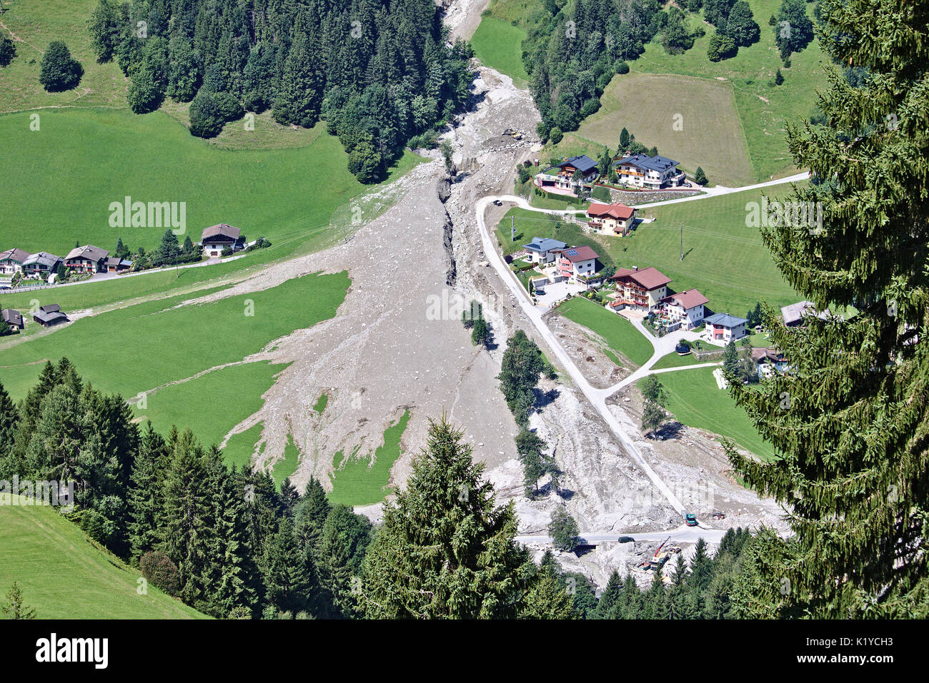 Luftaufnahme von Mountain Stream in den österreichischen Alpen blockiert nach einem massiven Schlammlawine mit Bagger und Lkw Reinigung und einem kleinen Dorf in der Nähe Stockfoto