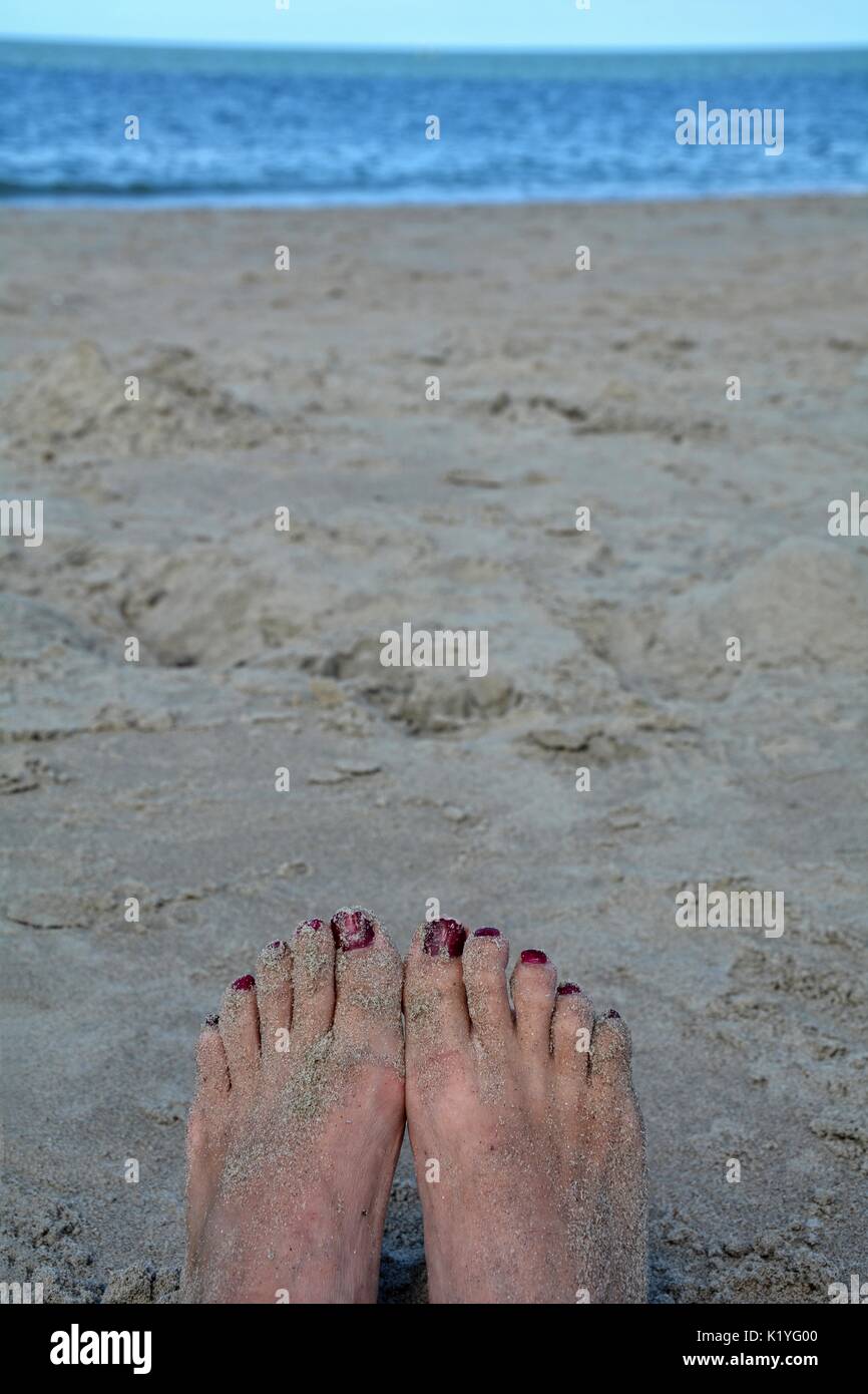 Sandy Füße mit roten Zehennägel am Strand mit verwischten Meer im Hintergrund Stockfoto