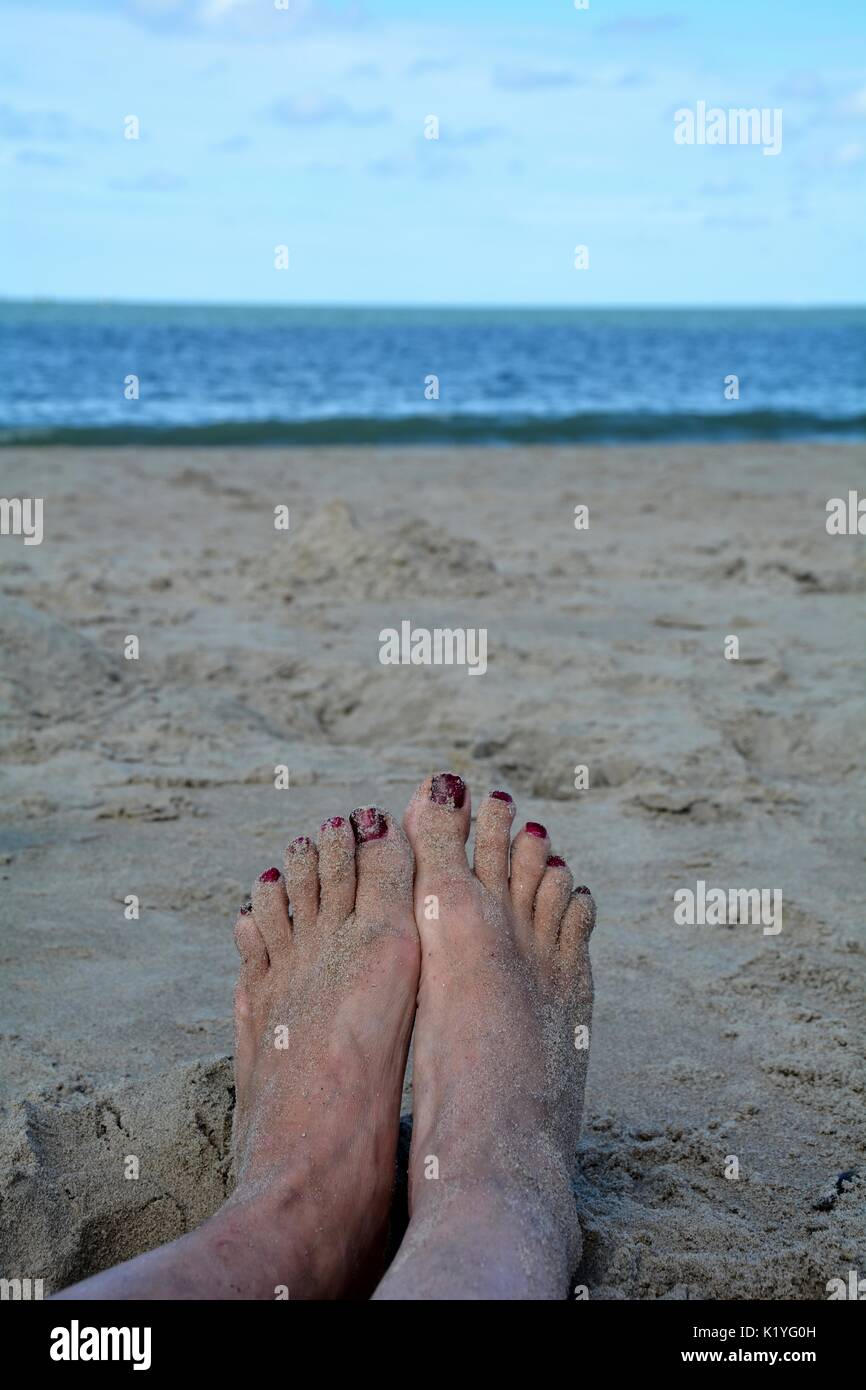 Sandy Füße mit roten Zehennägel am Strand mit verwischten Meer im Hintergrund Stockfoto