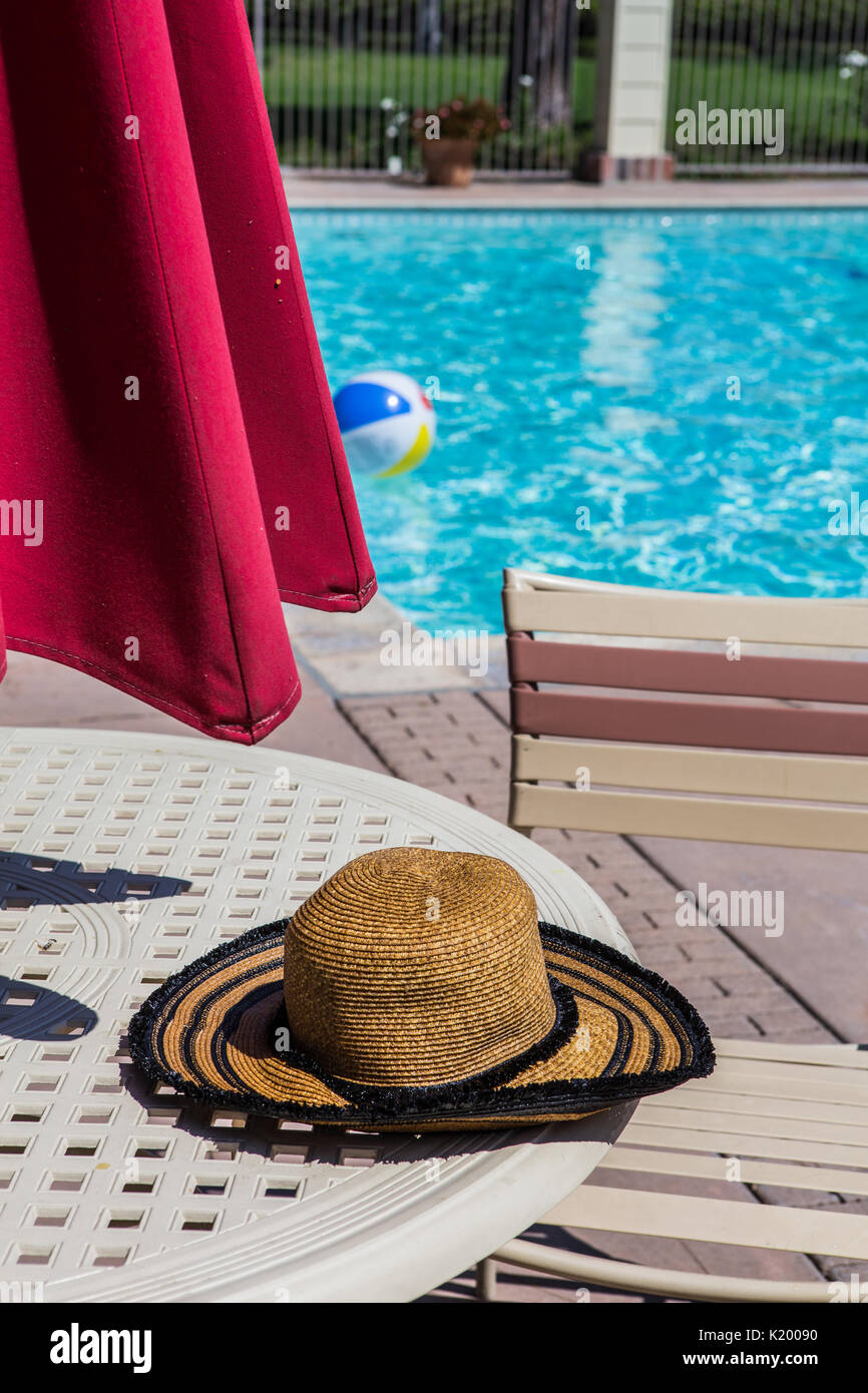 Womans Sommer Hut auf einem Tisch am Pool eines gemeinschaftlichen Pool mit einem bunten beachball Schwimmen in kristallklarem Wasser an einem heißen Sommertag Kalifornien Stockfoto
