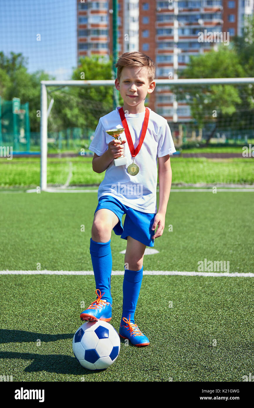 Sieger junge Fußballspieler mit Tasse und Goldmedaille auf dem Fußballplatz Stockfoto