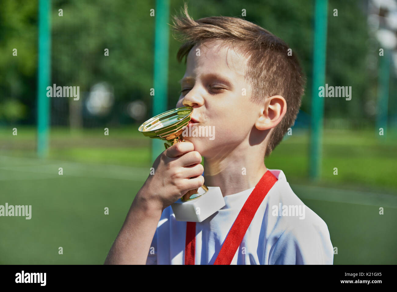 Sieger junge Fußballspieler küsse Cup auf dem Fußballplatz Stockfoto