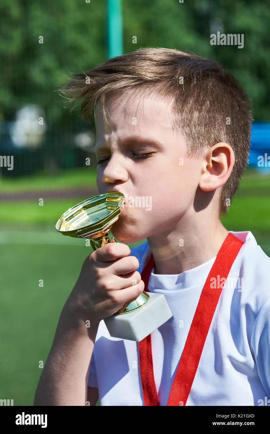 Sieger junge Fußballspieler küsse Cup auf dem Fußballplatz Stockfoto
