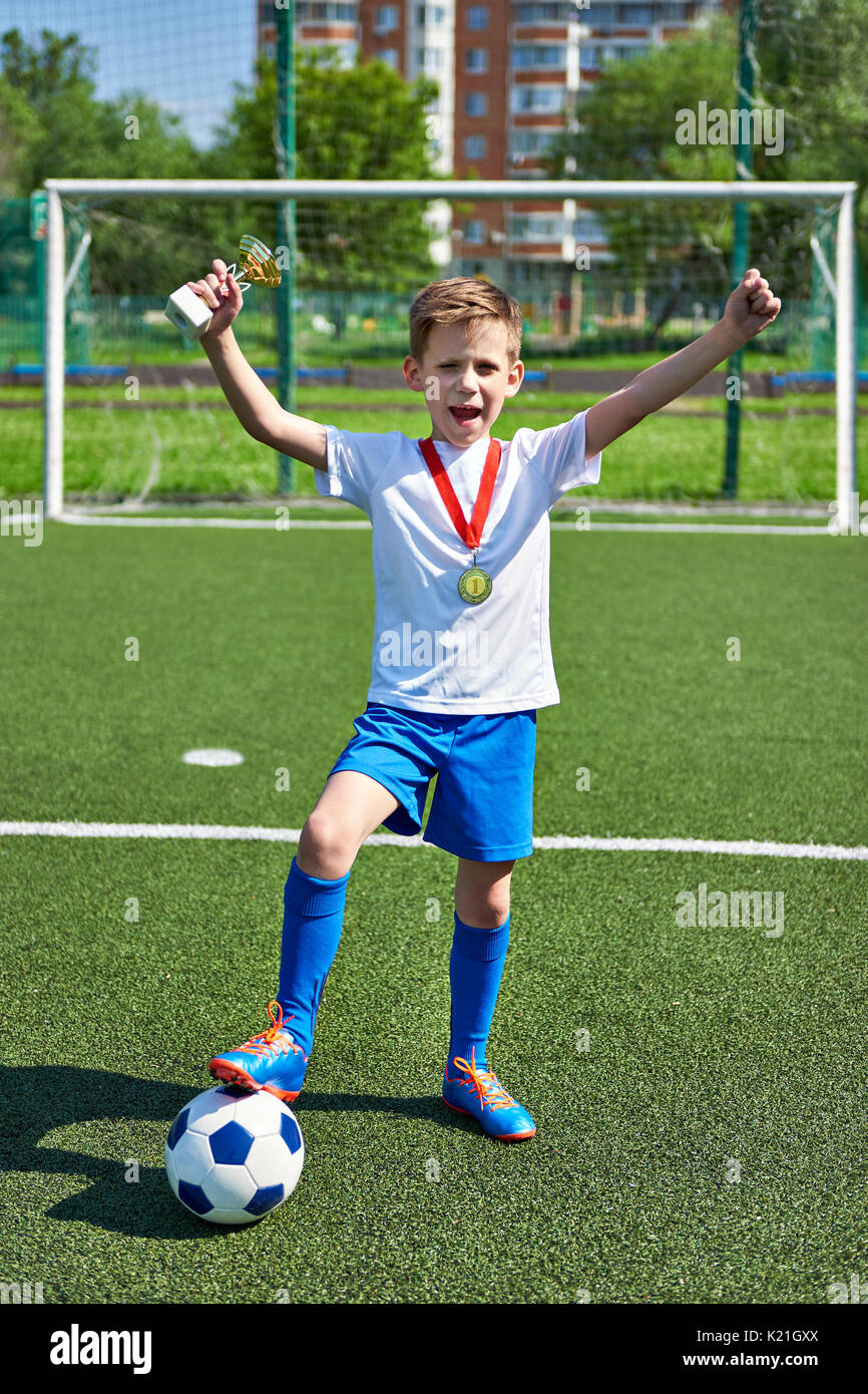 Sieger junge Fußballspieler mit Tasse und Goldmedaille auf dem Fußballplatz Stockfoto