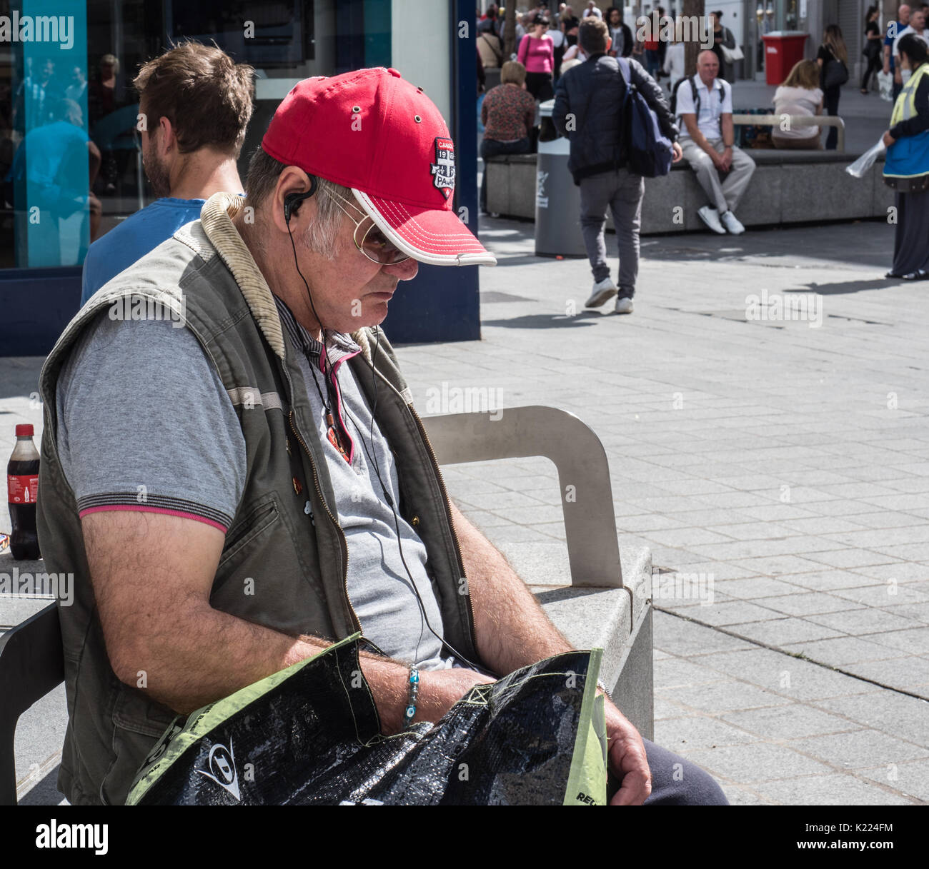 Mann sitzt auf der Bank mit Ohrhörer, Musik hören. Liverpool, England, UK Stockfoto