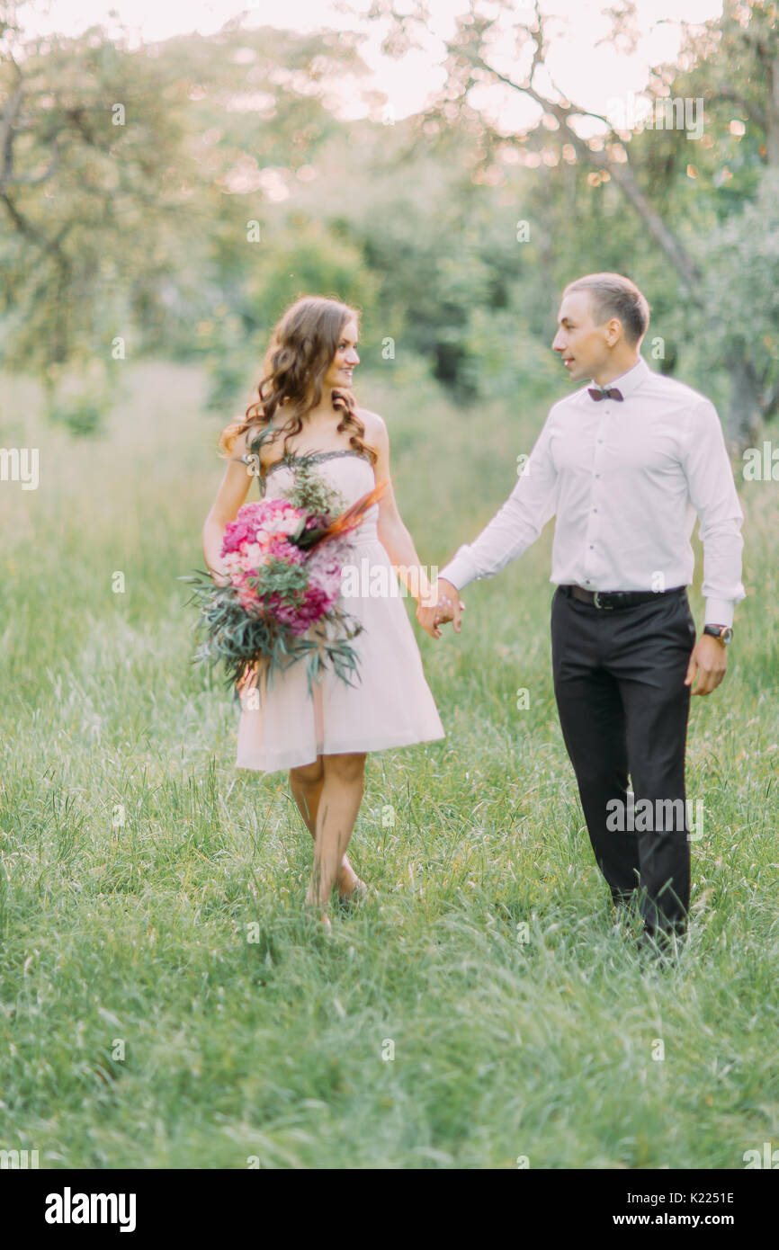 Das schöne Foto der Brautjungfer mit Blumen und der beste Mann ihre Hand Holding im sonnigen Wald. Stockfoto