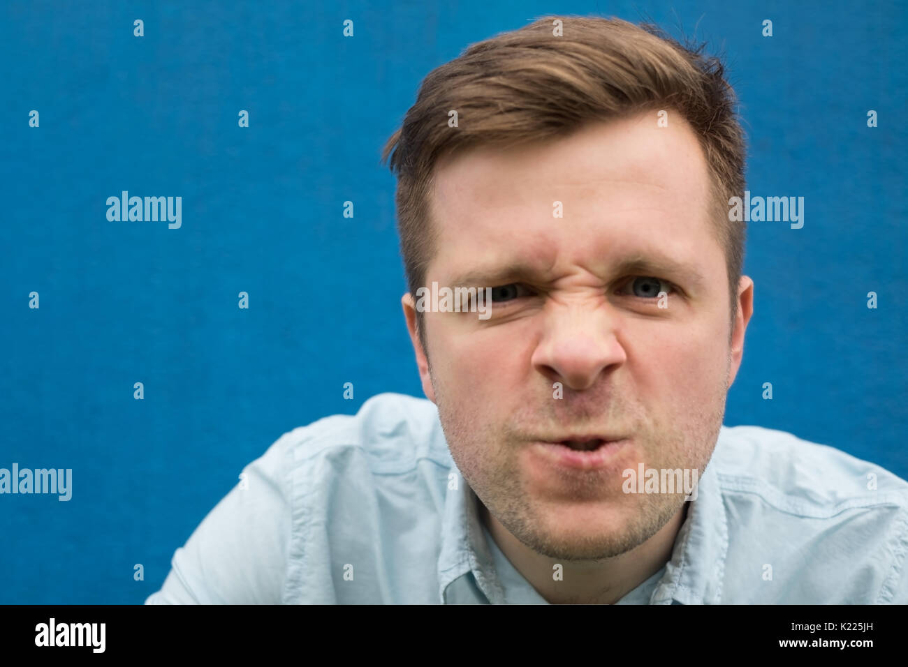 Angesichts einer zornig und wütend kaukasischen Mann auf einem blauen Hintergrund. Stockfoto