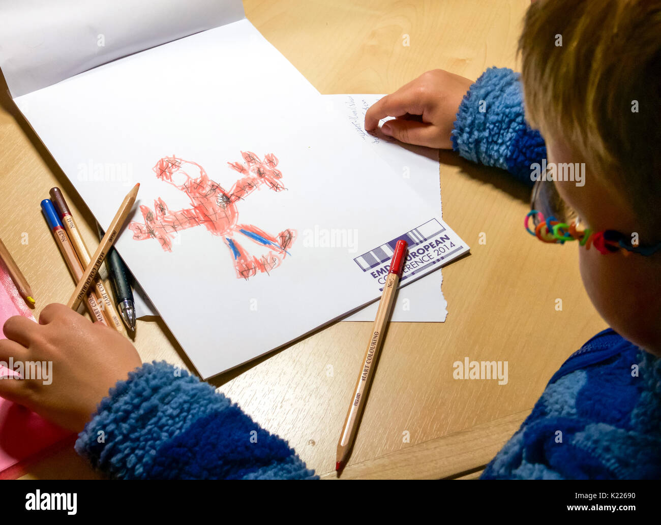 Junge mit Brille am Schreibtisch zu bewundern sein Bild von Spiderman mit Buntstiften auf Konferenz schrott Papier gezeichnet Stockfoto