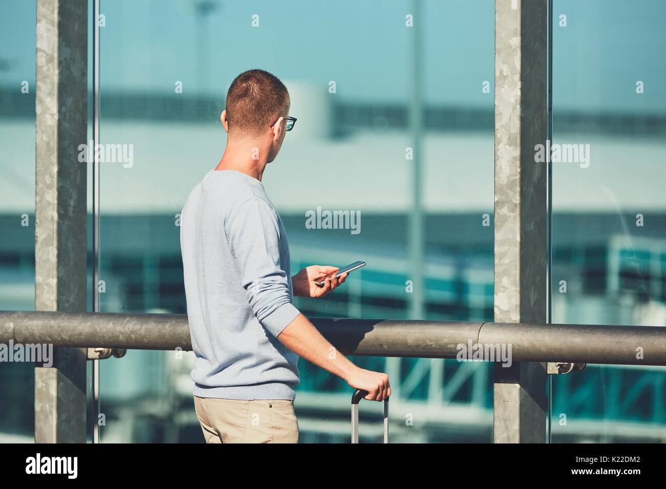 Mann mit dem Flugzeug reisen. Junge Reisende mit Handy am Flughafen warten auf einen verspäteten Flug. Stockfoto