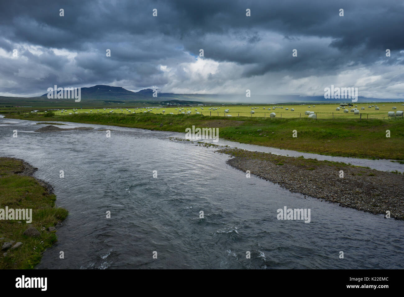 Island - Hunderte von Strohballen hinter dem Fluss auf der grünen Wiese mit intensivem Regen Wolken und der Traktor während Gewitter Stockfoto