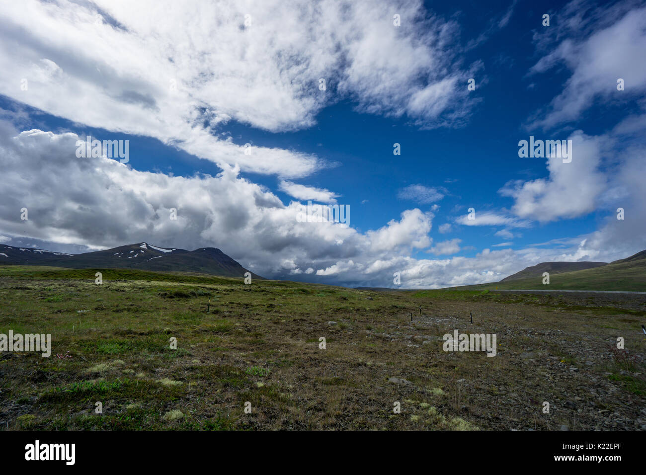 Island - Blauer Himmel mit Sonne und Wolken mit Gewitter über grüne Landschaft Stockfoto