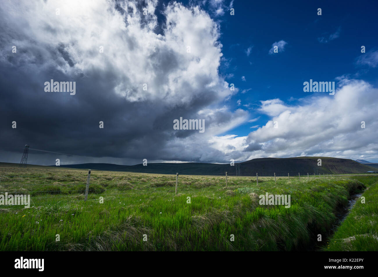 Island - Fluss mit grüner Wiese und dunklen Gewitterwolken zu kommen, wie die Sonne scheint Stockfoto