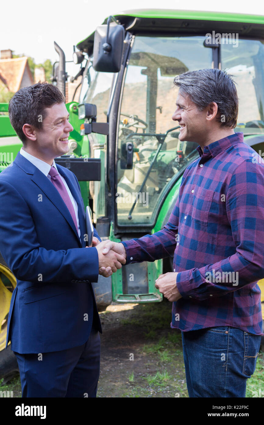 Landwirt und Geschäftsmann Händeschütteln mit Traktor im Hintergrund Stockfoto