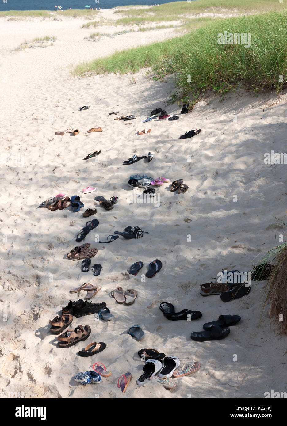 Sandalen, Flip Flops und Schuhe in den Sand links von barfuß Beachgoers. Stockfoto