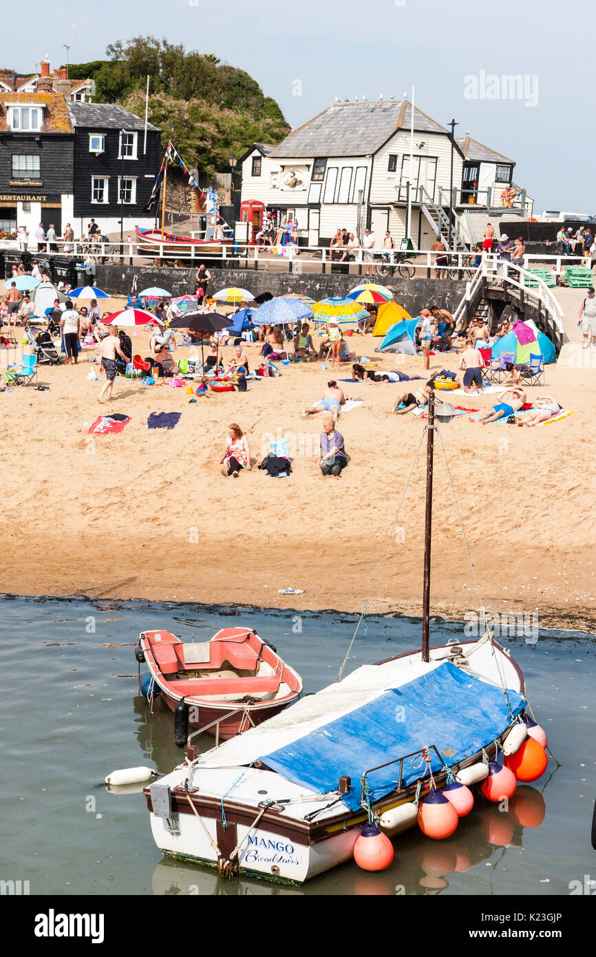 England, Viking Bay, Broadstairs. Strand total vollgepackt mit Sun Asylbewerber während der heißen Wetter. Der Strand und das Meer im Blick, Massen von Menschen am Strand. Strahlender Sonnenschein. Angeln Boot im Vordergrund und das Wahrzeichen der alten Rettungsboot das Weiße Haus im Hintergrund. Stockfoto
