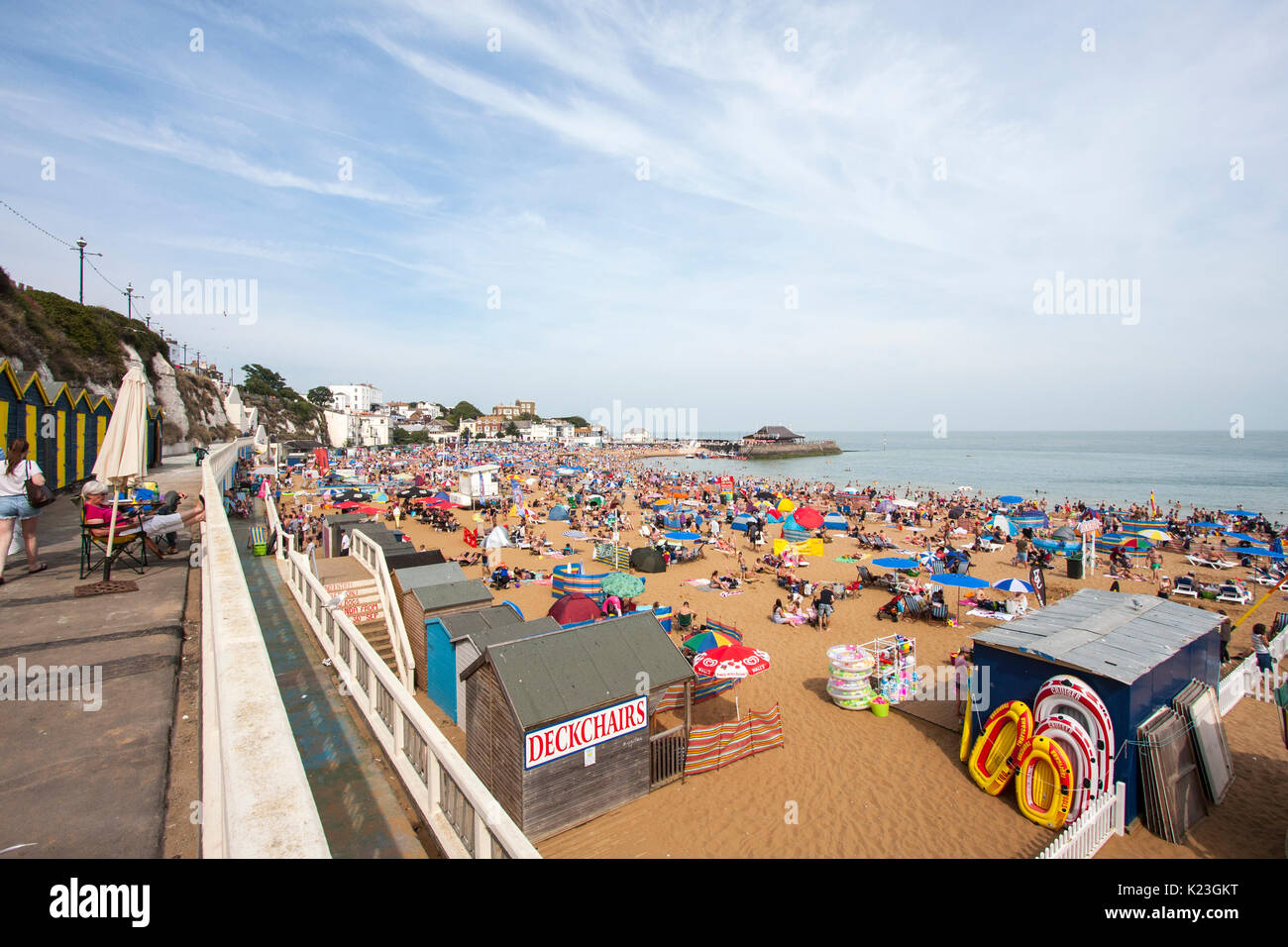 Blick entlang Badekabinen, Balkon Promenade, Strand und Broadstairs Hafen. Hitzewelle im Sommer, Strand überfüllt mit Sonnenanbeter. Blauer Himmel, ruhige See. Stockfoto