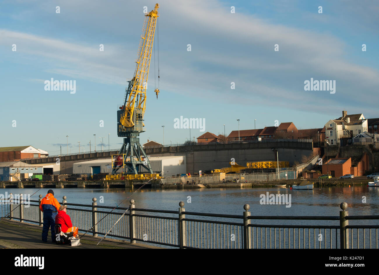 Fischer, die Rod und Linie entlang der Hafenseite und des Flusses nutzen, tragen in der Stadt Sunderland mit einem großen Kran am Flussufer im Hintergrund Stockfoto