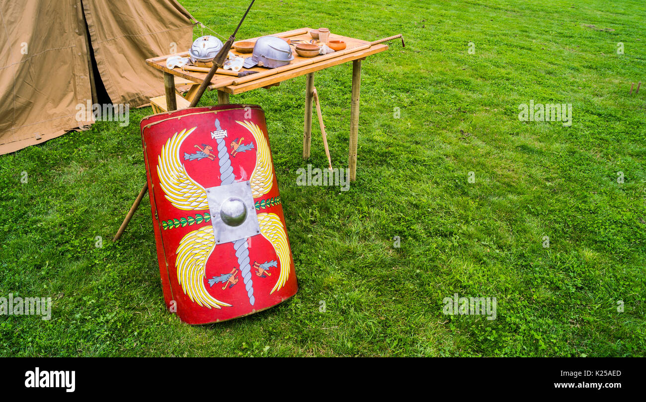 Ausrüstung eines römischen Soldaten (römischer Schild, Speer, römischer Helm) auf einem Holztisch auf einem grünen Grasfeld und einem Zelt im hinteren Boden verstaut Stockfoto